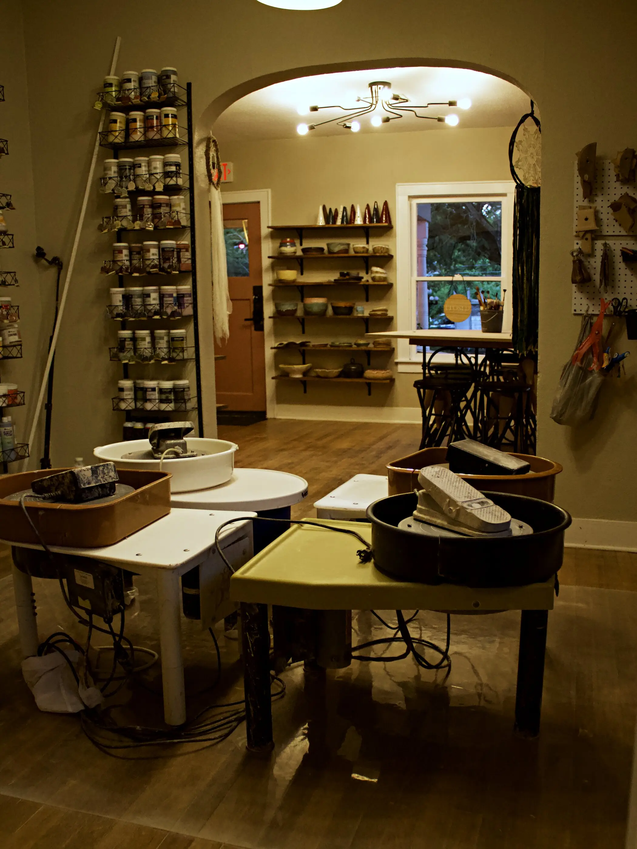 Inside the studio — pottery wheels at worktables, with shelves of glazes and greenware in the room beyond